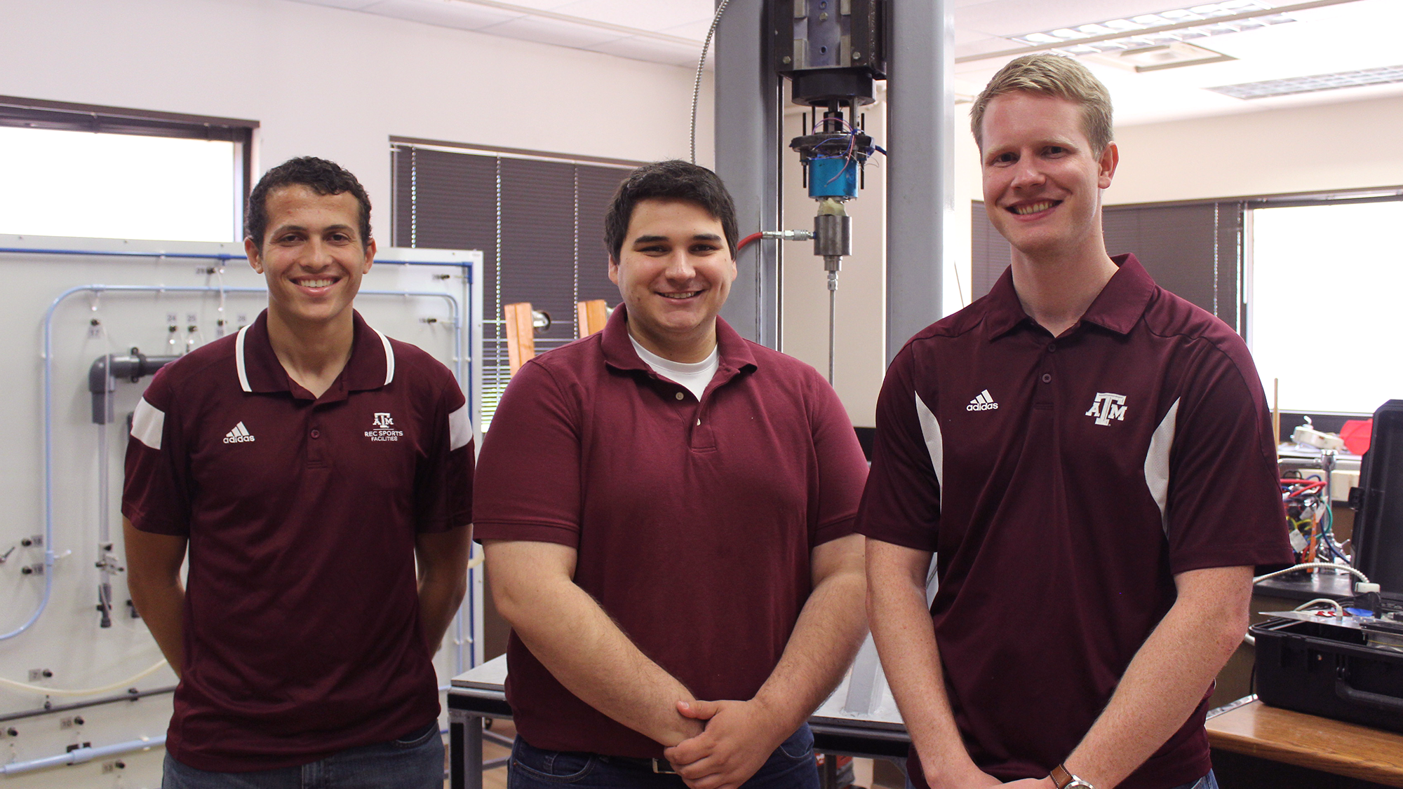 three students pose with their small-scale drilling rig