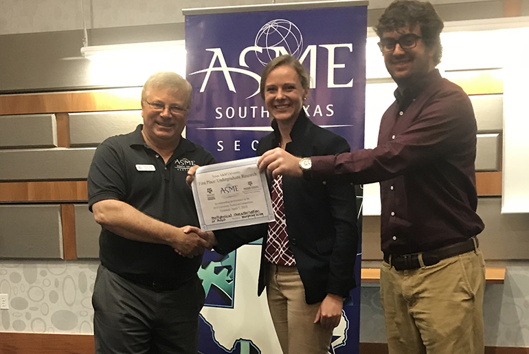 Two students (one male and one female) with an older male. The female student is shaking hands with the man and the male student (who is standing beside her) is reaching across her and holding one corner of the award certificate.