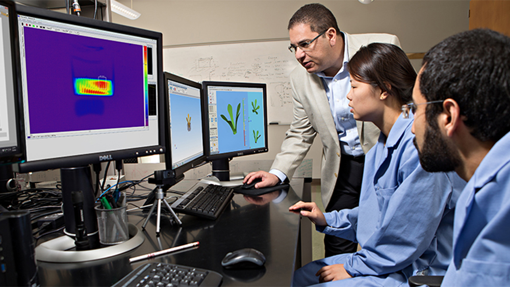 Dr. Alaa Elwany looks at a computer with two students. 