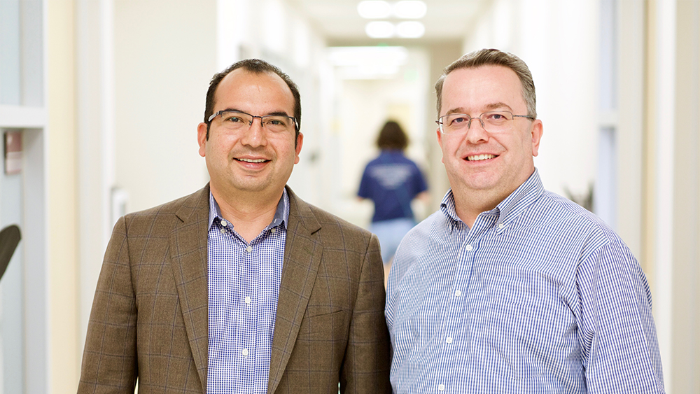 Dr. Arroyave and Dr. Karaman stand beside each other in a hallway. 