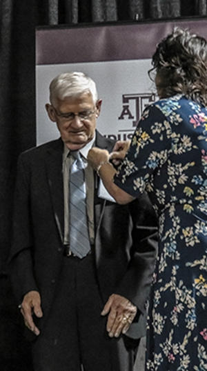 Dr. Koppa has a lapel pin put on his jacket by another individual. 