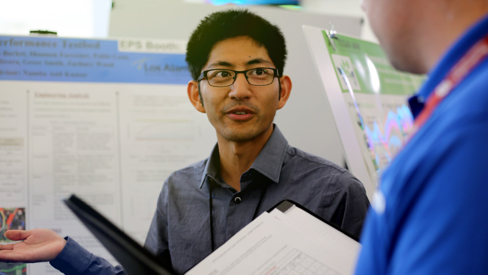 A male engineering student looking at the industry judge and gesturing to his product.