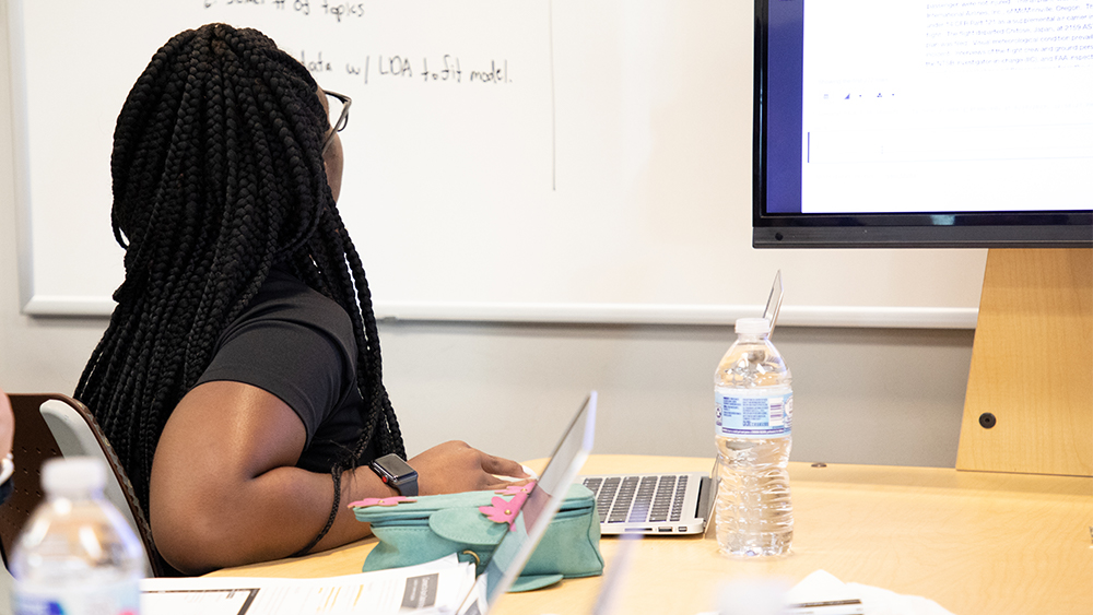 Student looks at a computer screen and whiteboard. 