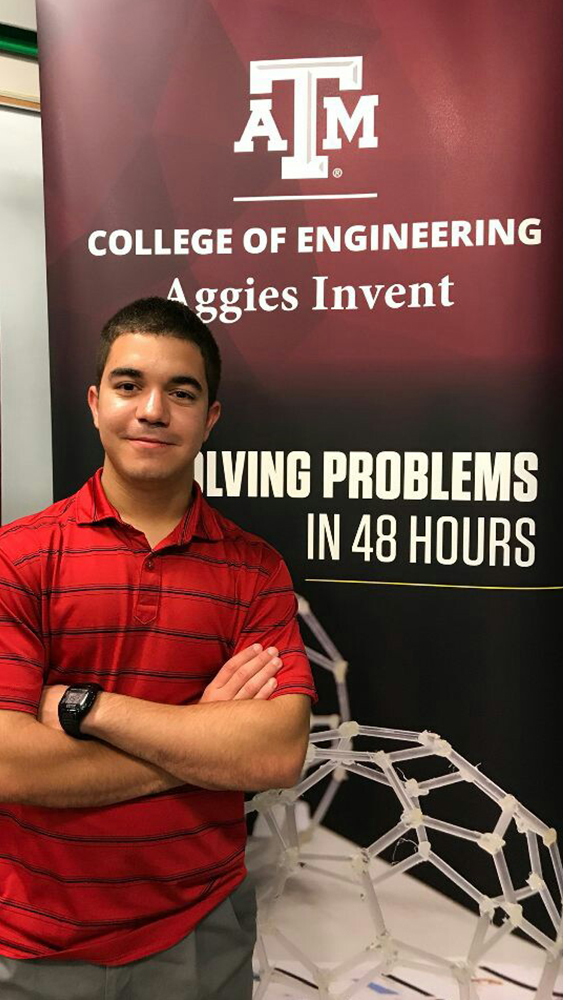 Hector Garcia stands with arms folded in front of a poster that says "Aggies Invent."