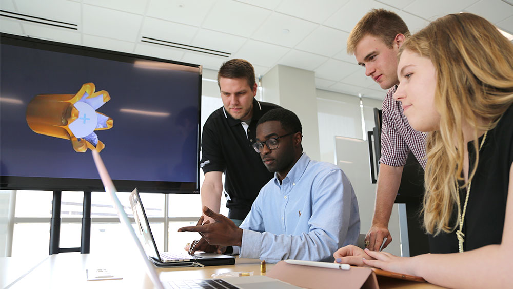 four students work on a project around a desk