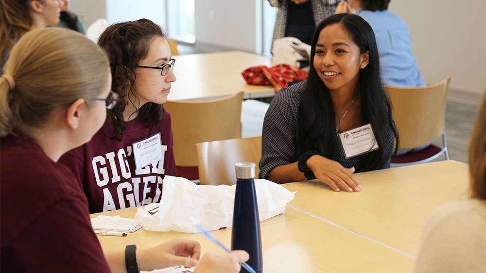 Three female students sitting together talking. One student with a maroon shirt on that says GIG'EM AGGIES