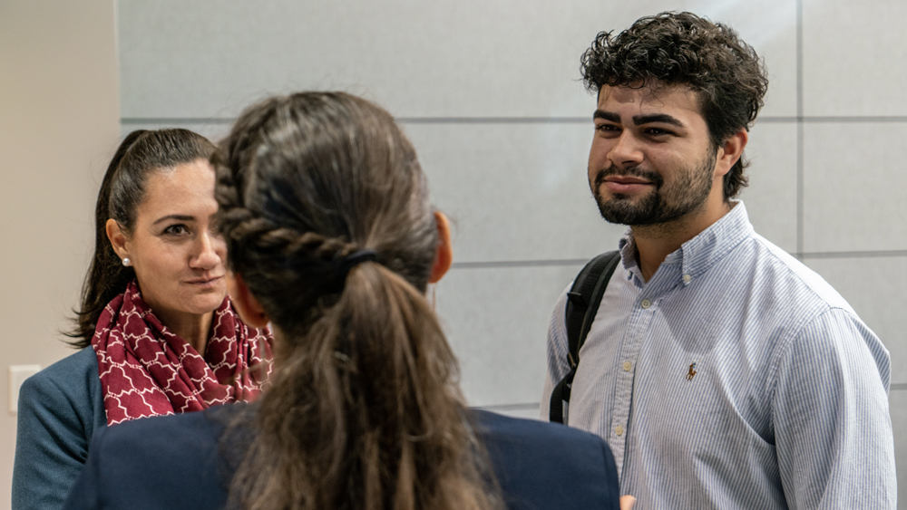 A man and woman with brown hair chat with a woman with brown hair who is turned away from the camera.