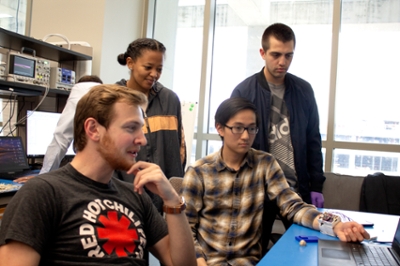 Students watch the results of a blood pressure cuff on a laptop screen.