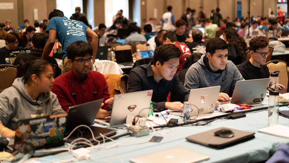 Four students seated at table working their on laptops during the TAMUhack event.