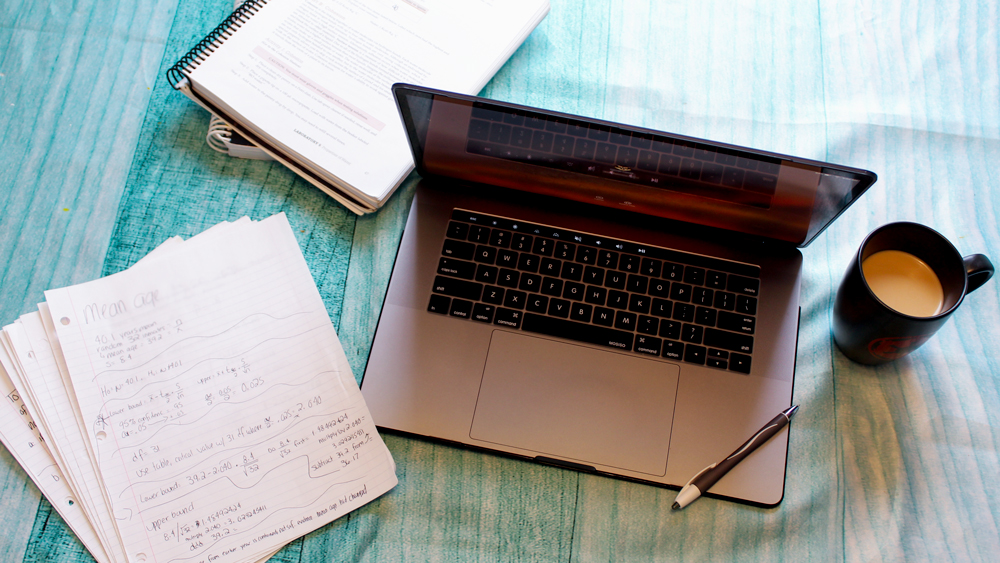 A laptop, two textbooks and a stack of school notes on a table