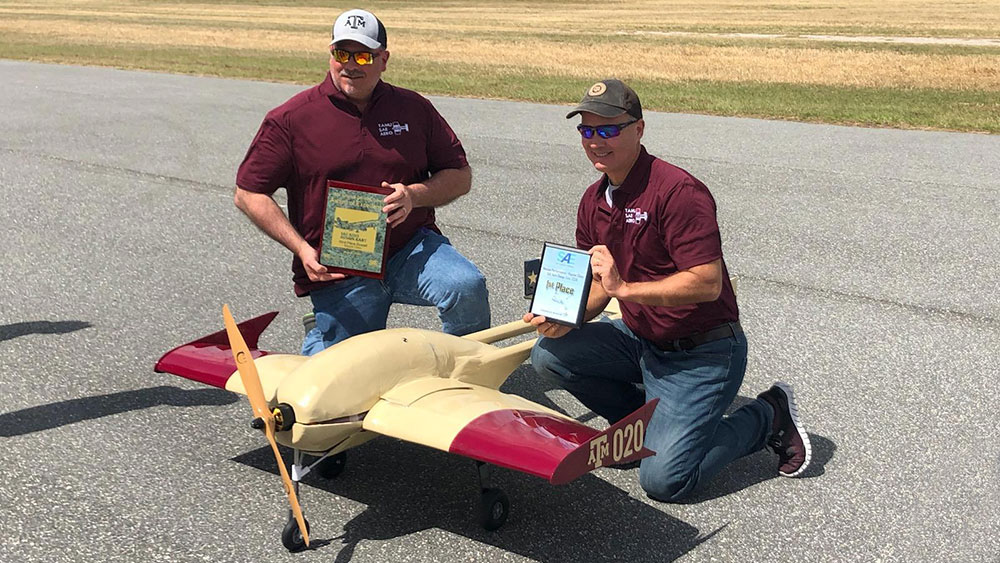 Scott McHarg and Brad Worsham, SAE advisors, holding awards and posing on runway next to team's aircraft.