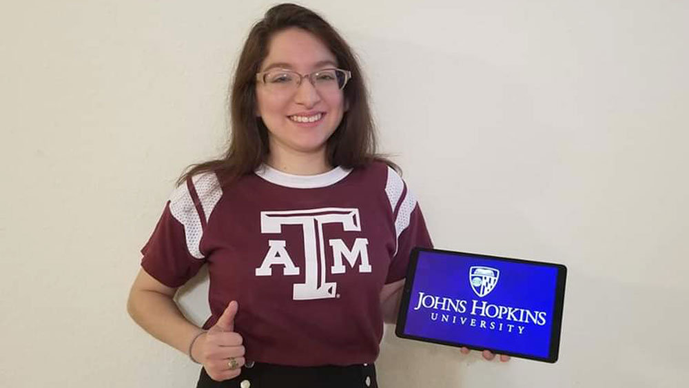 Amanda Rakoski grinning and holding a tablet that displays her chosen graduate school: Johns Hopkins University.