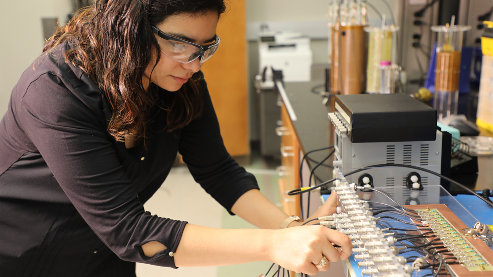 Female student wearing safety goggles working with wired equipment.