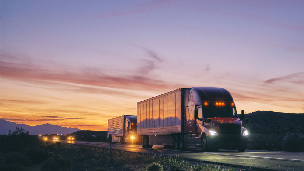 Large semi truck hauling freight on the open highway under an evening sky.