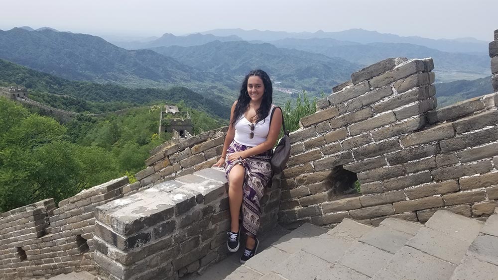 Alarcon poses against the Great Wall of China overlooking vibrant and lush mountains covered by fog.