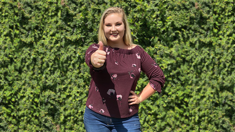 Julia Reed standing in front of a bush giving a thumbs up