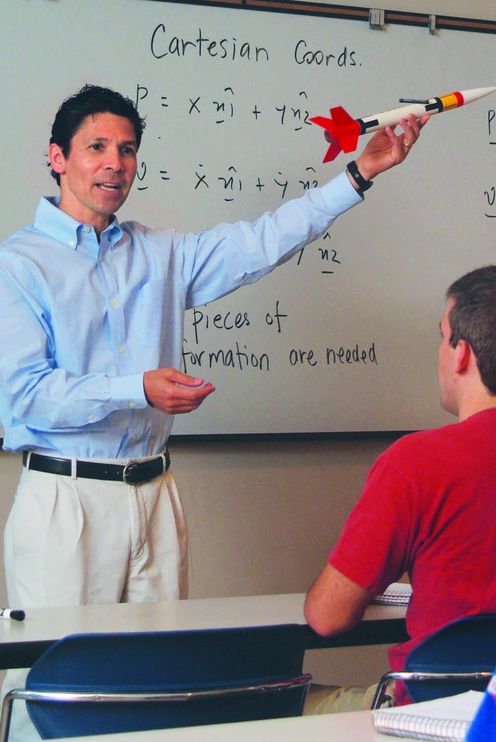 Dr. Hurtado stands at the front of a classroom holding a rocket in the air