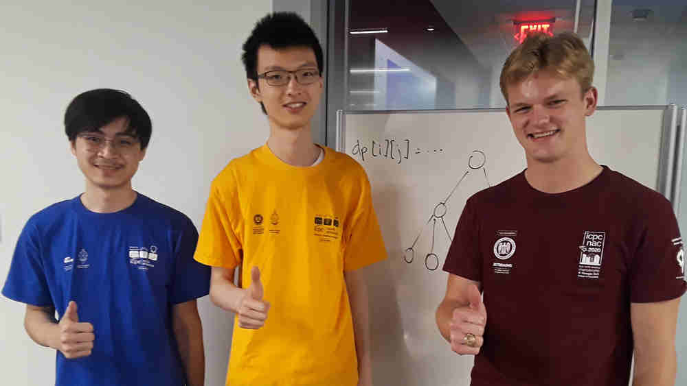 Three male Texas A&M students in a meeting room, standing in front of the whiteboard. All are smiling at the camera and giving a thumbs up.