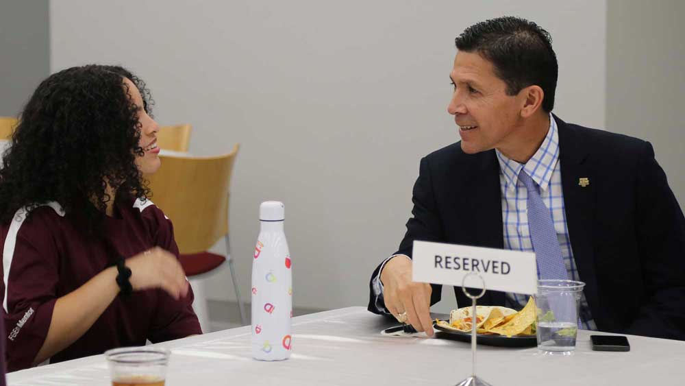 A man and woman sitting at a table, speaking to each other.