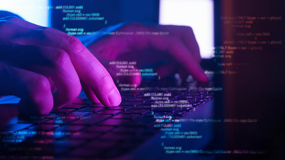 Close-up of hands typing on keyboard with lines of computer code in the background.