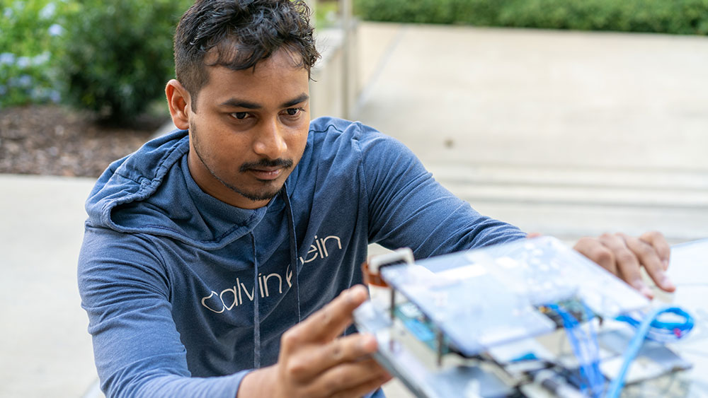 Santosh Ganji squatting next to his antenna on a rolling cart