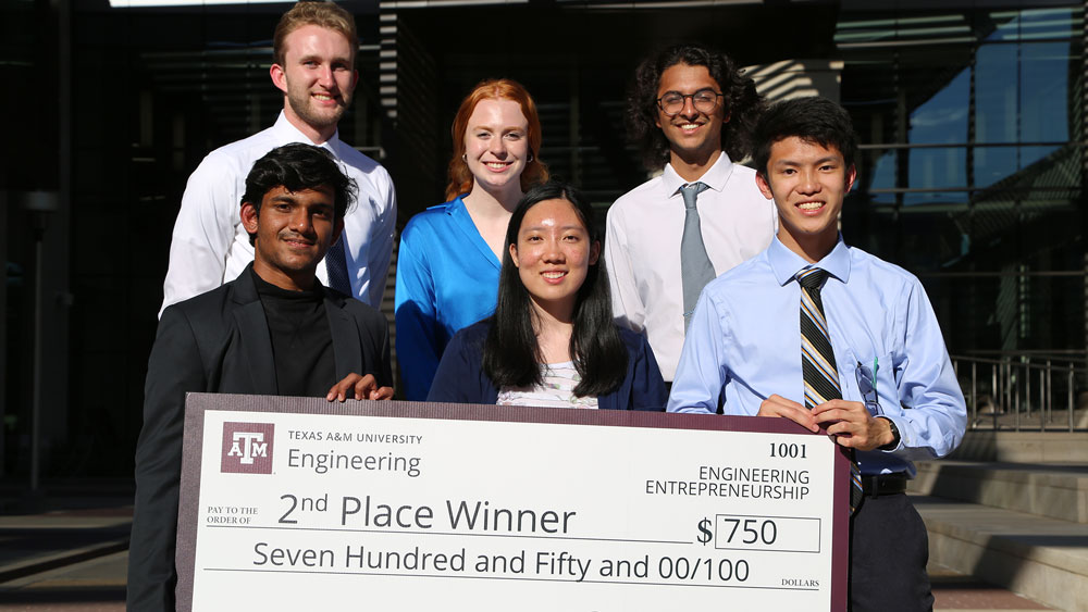 Six members of second-place team Up to Data holding a large sign representing a check awarded to them for $750.