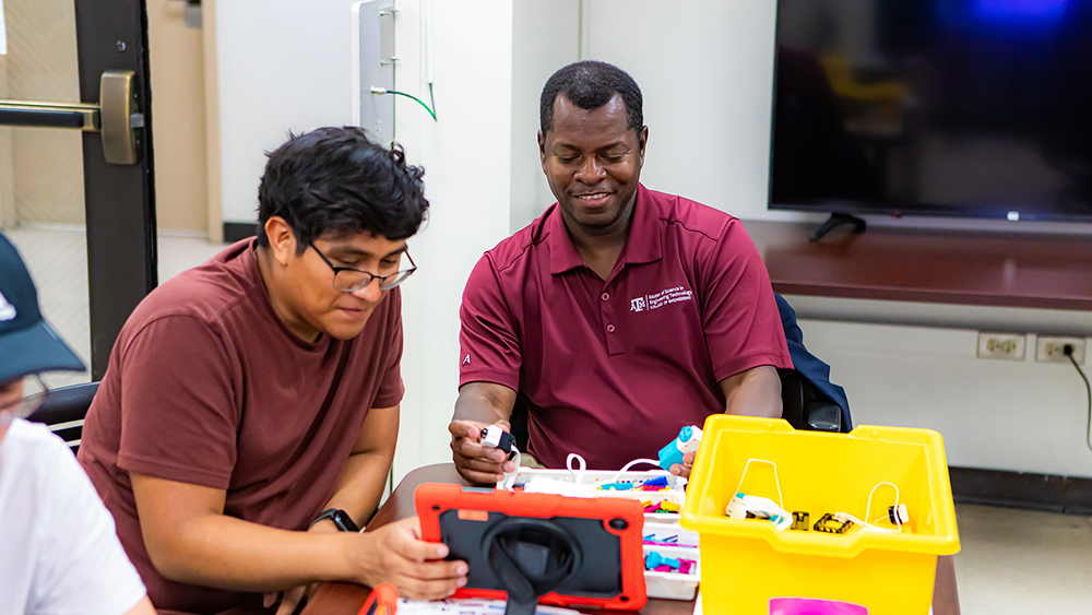 Dr. Crosby and student interacting with the robotics programming interface with a Lego robotics kit on a table.