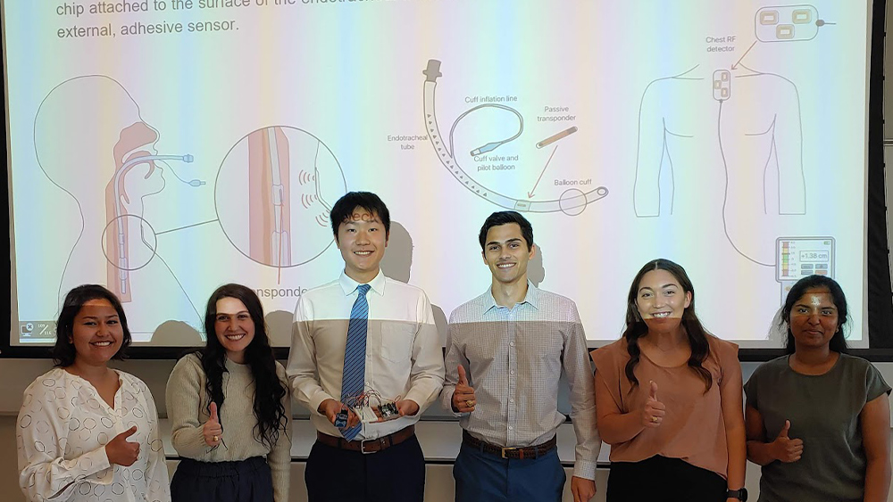 Six students stand in front of a board with information on their capstone project. 