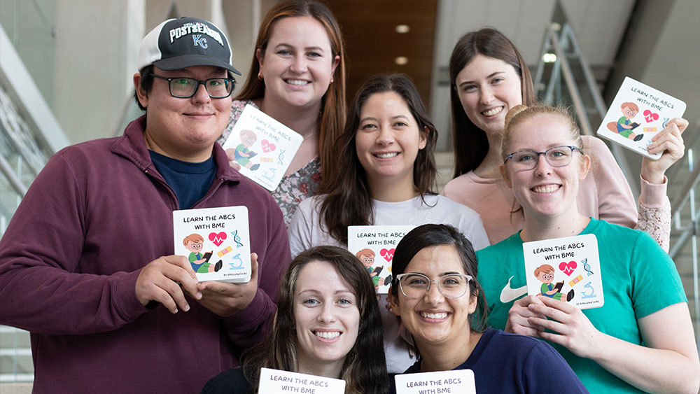 Student authors from biomedical engineering stand on a staircase, each holding a copy of Learn the ABCs with BME.