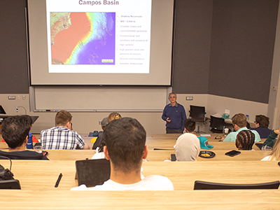 Dr. Mauro Becker, standing in front of wall screen, gives presentation to seated students.