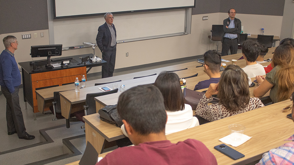 Three men, Dr. Mauro Becker, Dr. Cesar Palagi and Dr. Ibere Alves, standing in front of a group of seated graduate students.