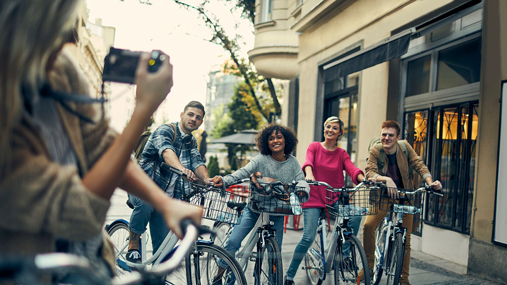 A woman taking a photo of her friends on a bike ride in a city. 