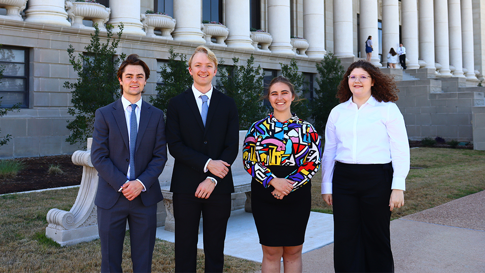 Students stand in front of a building with pillars at Texas A&amp;M University.