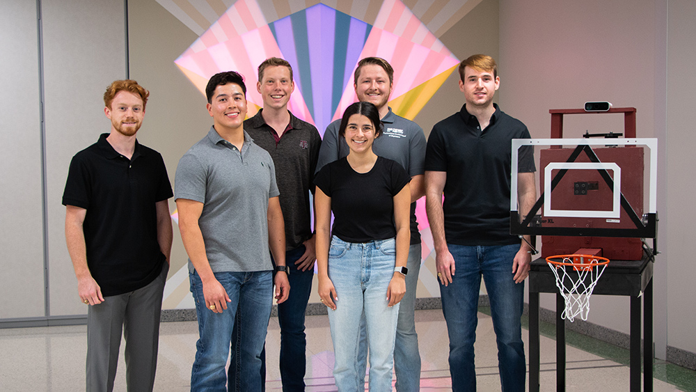 Six mechanical engineering students posing with their prototype backboard and hoop system.