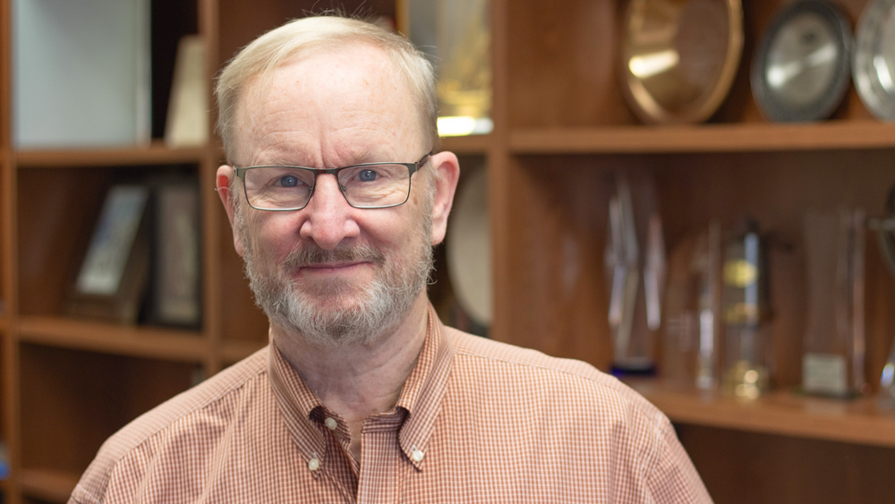 Dr. D. Nathan Meehan wearing glasses and standing in front of a bookcase littered with books and awards.