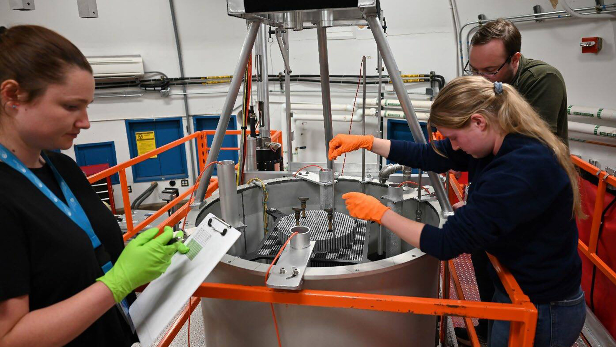 Three people wearing gloves in a lab with a nuclear core reactor.