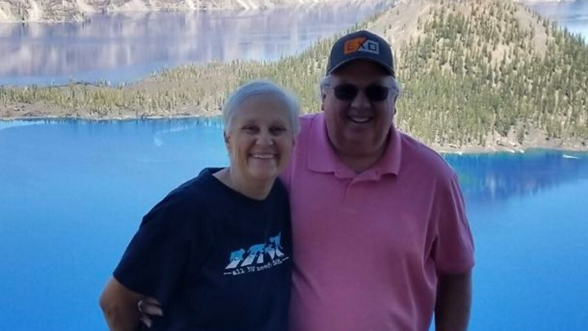  Denise and Wesley Oliphant smiling at the camera in front of a lake and mountains.