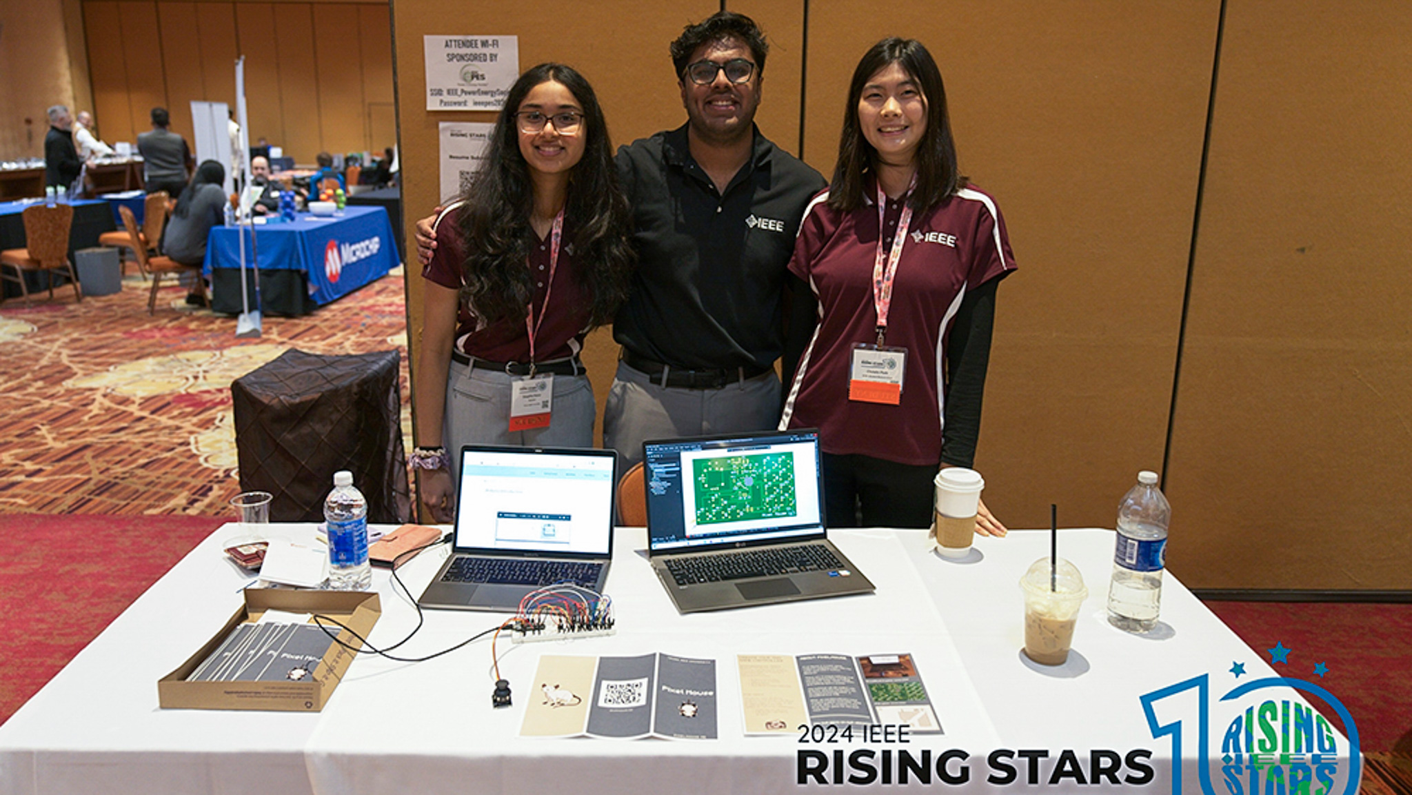 Deeptha Karur, Karthik Ravikumar and Christin Park standing and smiling at their Pixel Mouse table on the first day of the conference. 