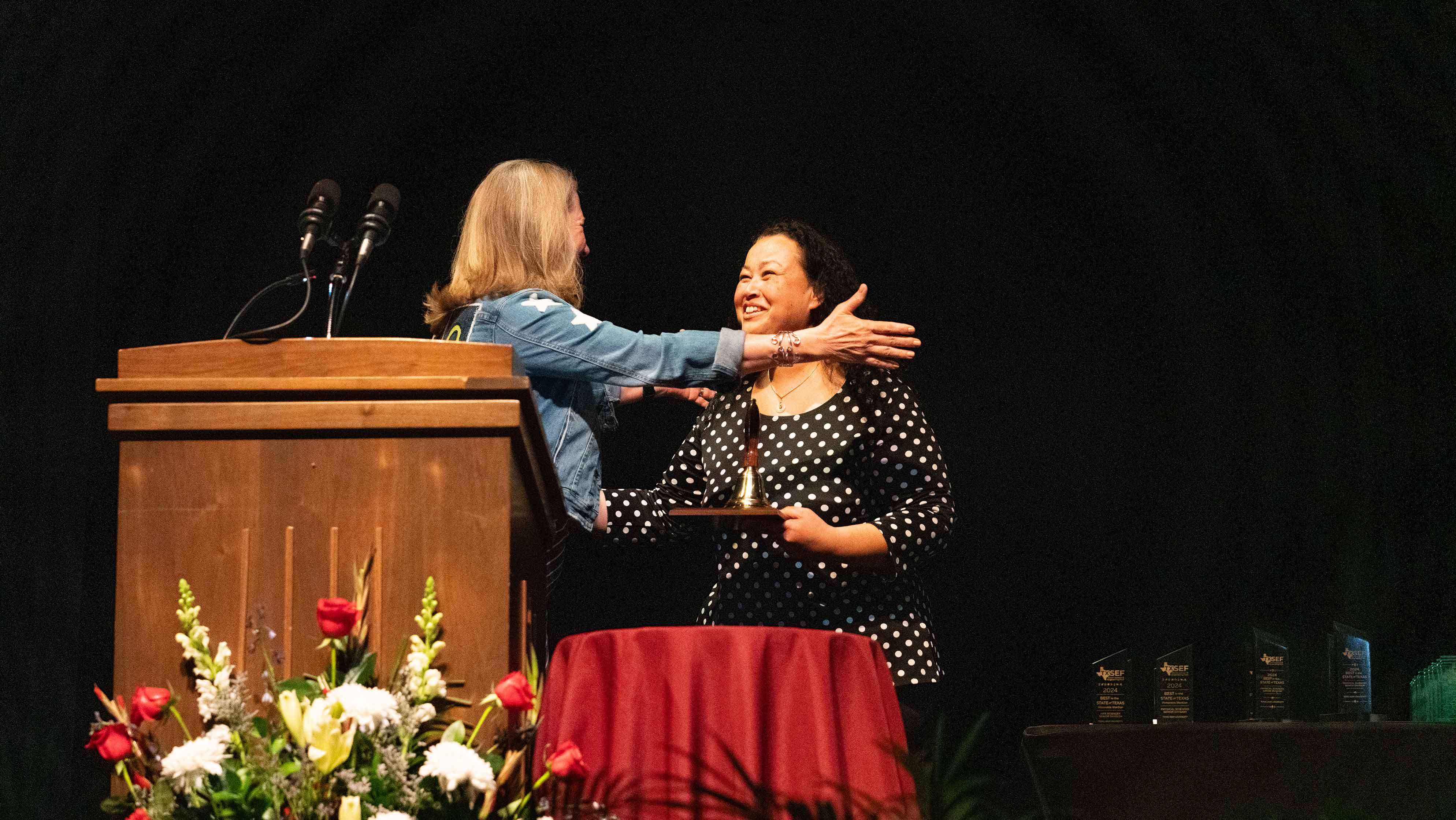  Two women embracing at a podium.