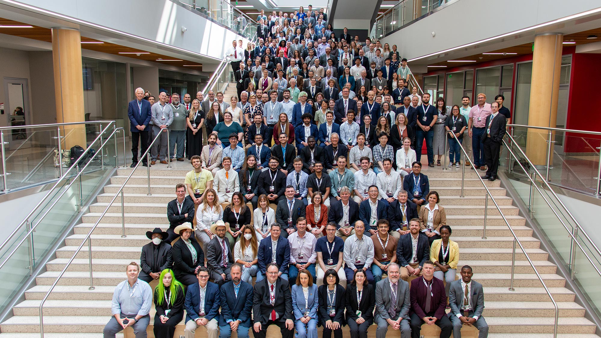 More than 250 people, wearing business attire and conference lanyards, sit on a wide set of stairs.