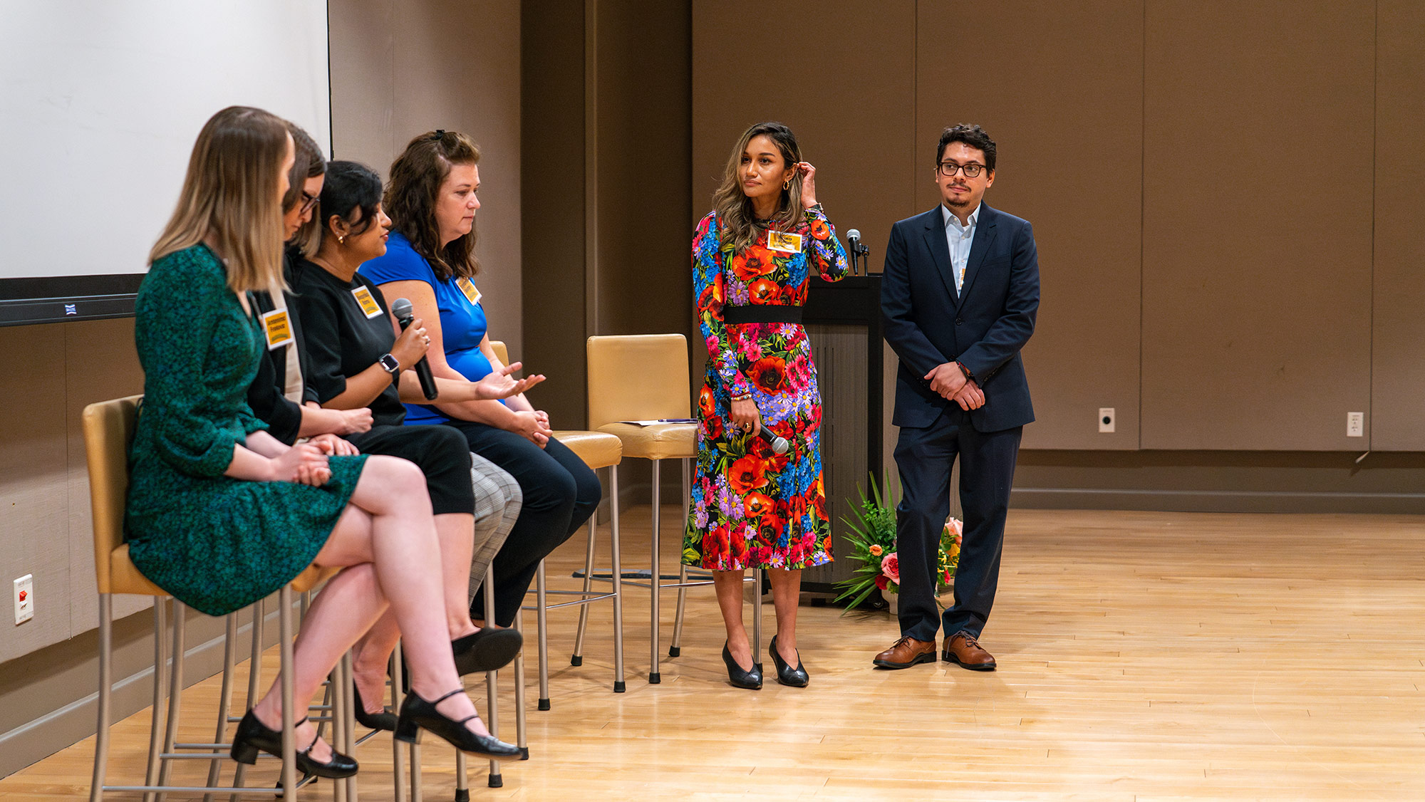 Four people sitting in chairs with one speaking into a microphone with two others standing next to them.