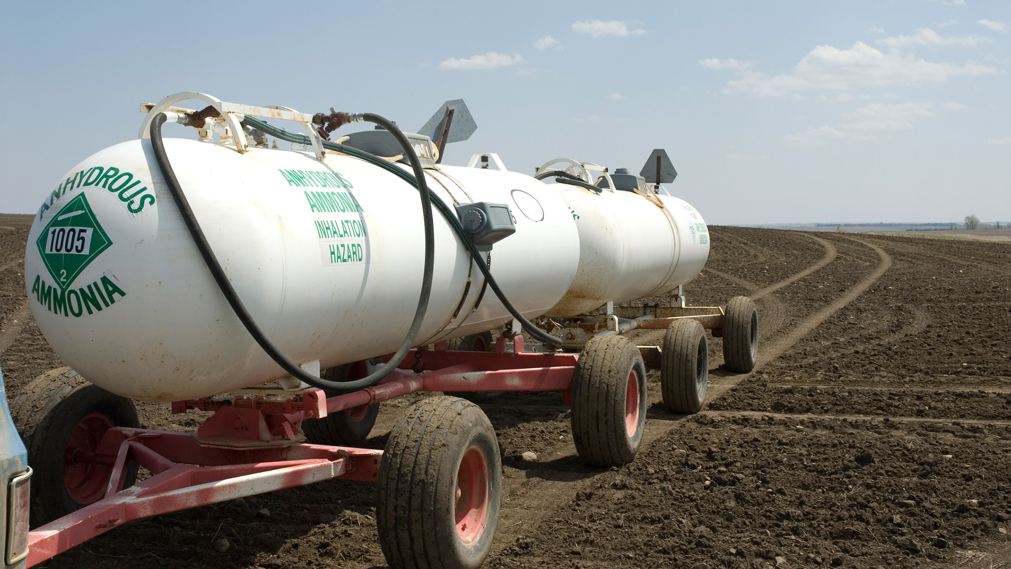 White tanks of ammonia being transported through a dirt field.