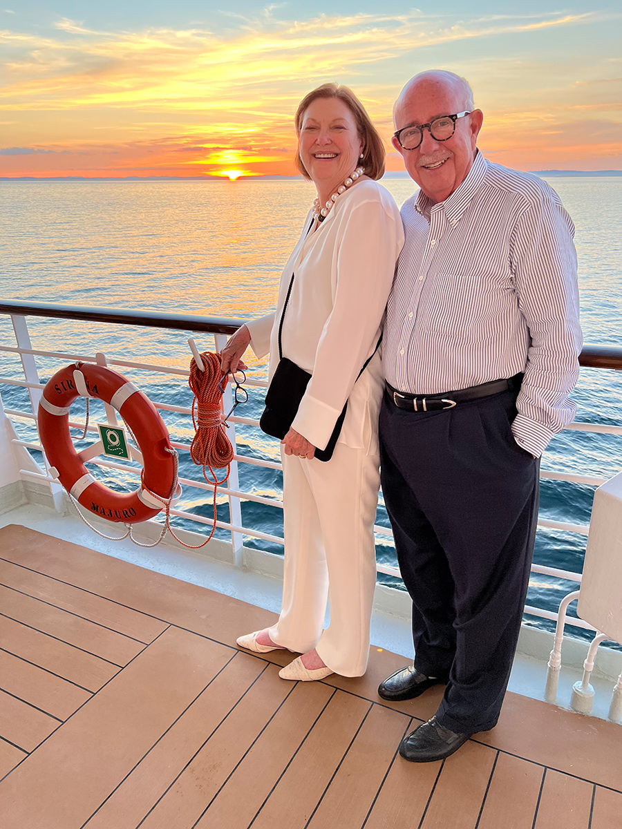  Man and woman on a cruise ship smiling in front of a sunset. 