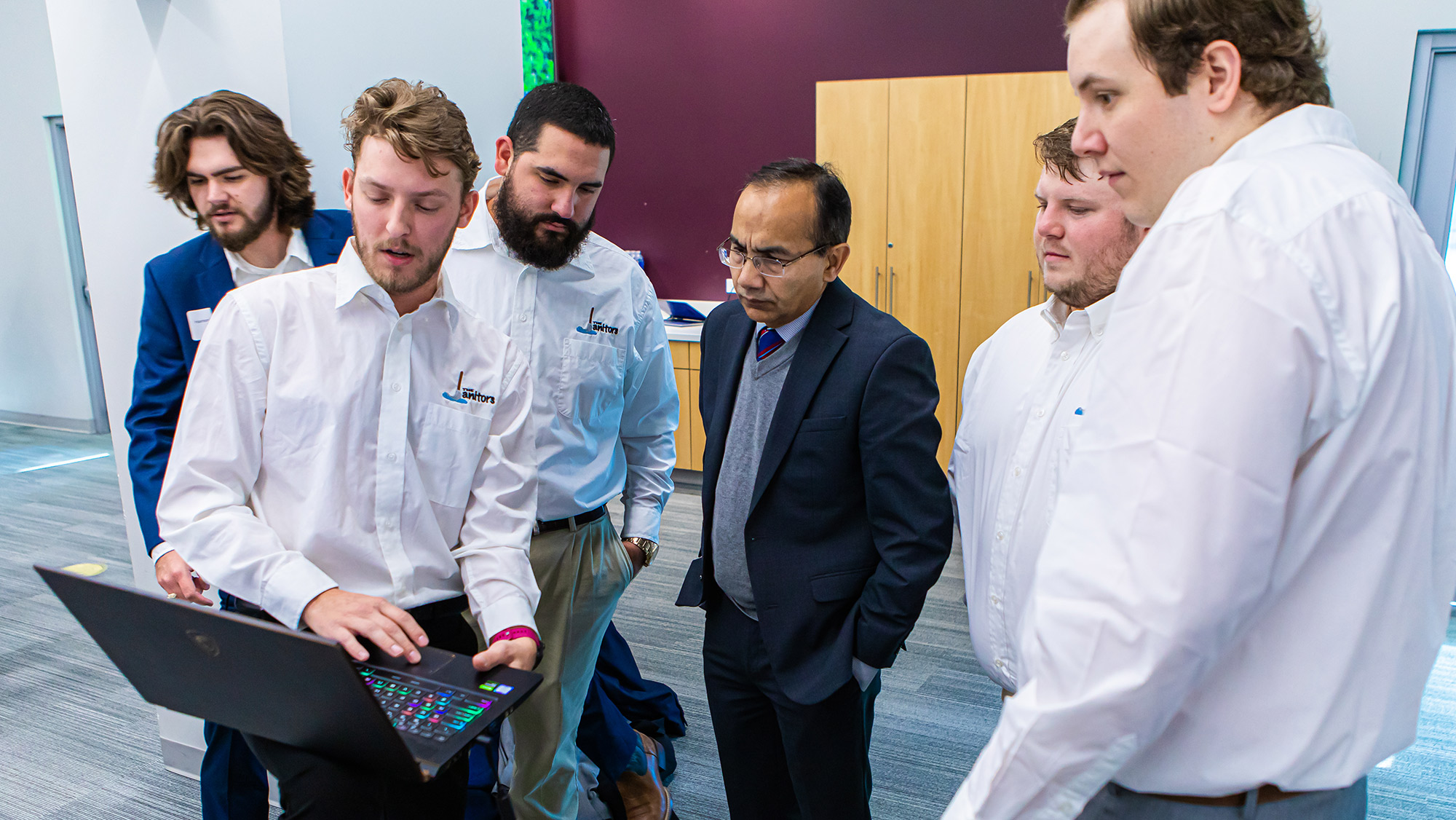 A man holding a laptop computer explains a concept to five individuals.