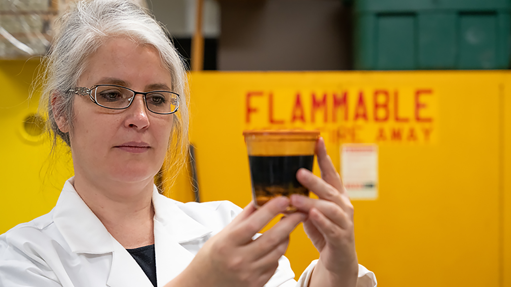 A woman looks at beaker of oil in laboratory.