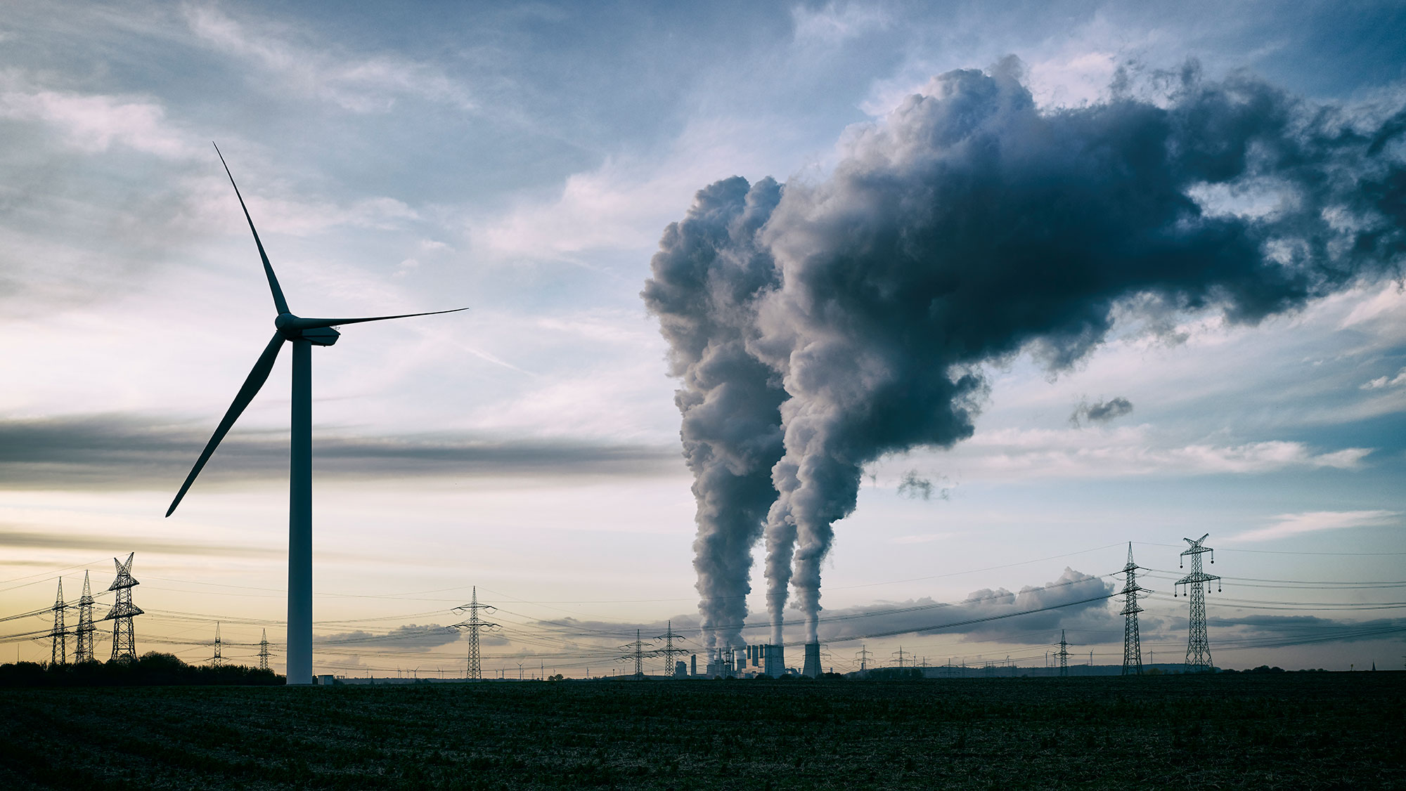 Single wind turbine, a coal-burning power plant with pollution and electricity pylons in the background