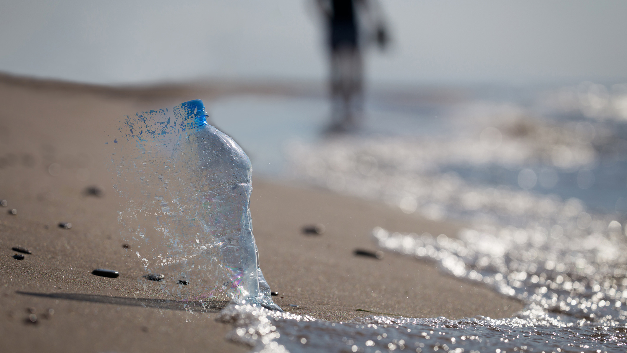 A plastic bottle dissolving into water on the beach.