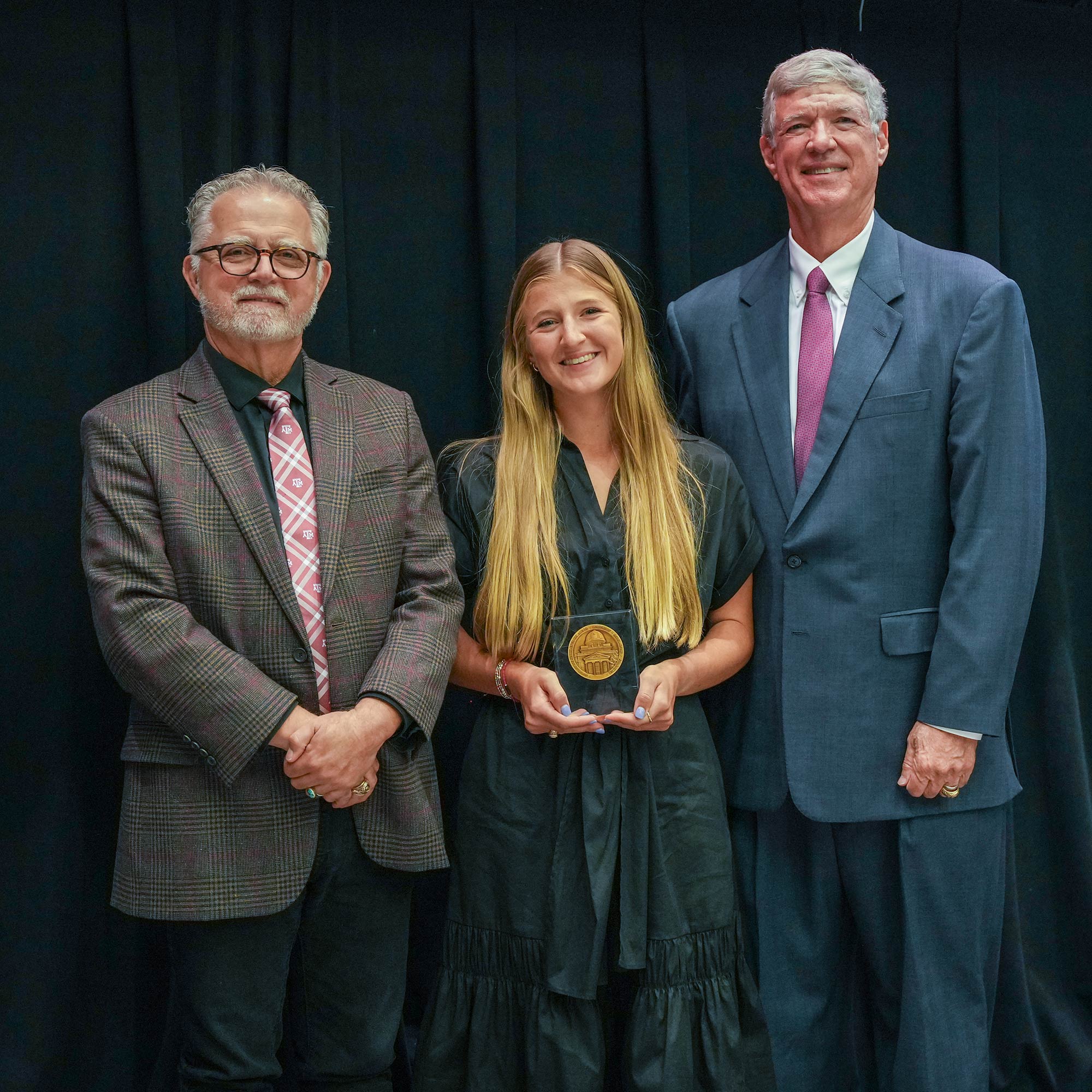 Two men standing next to woman with an award.