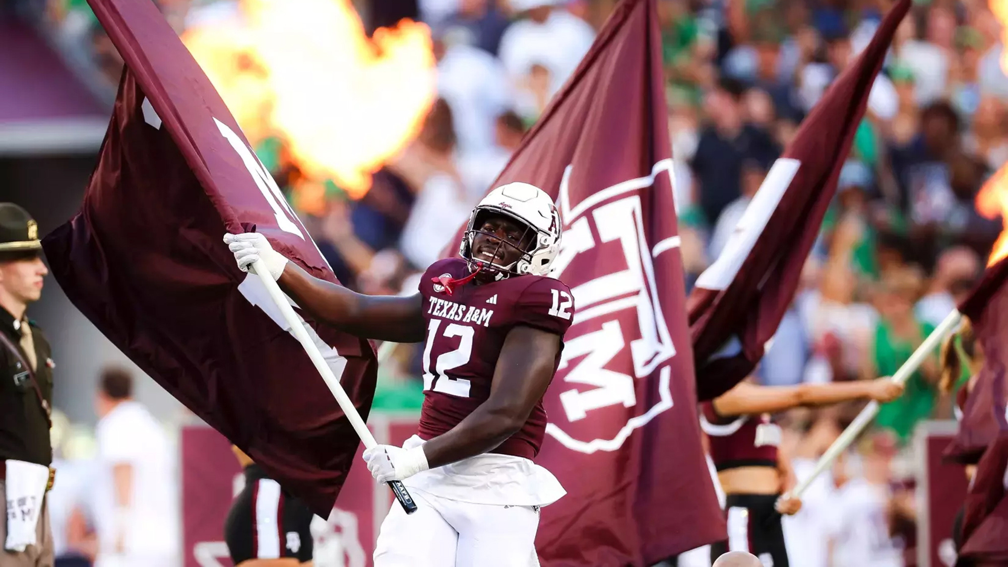 A football player in a maroon jersey waving a flag runs on a football field.