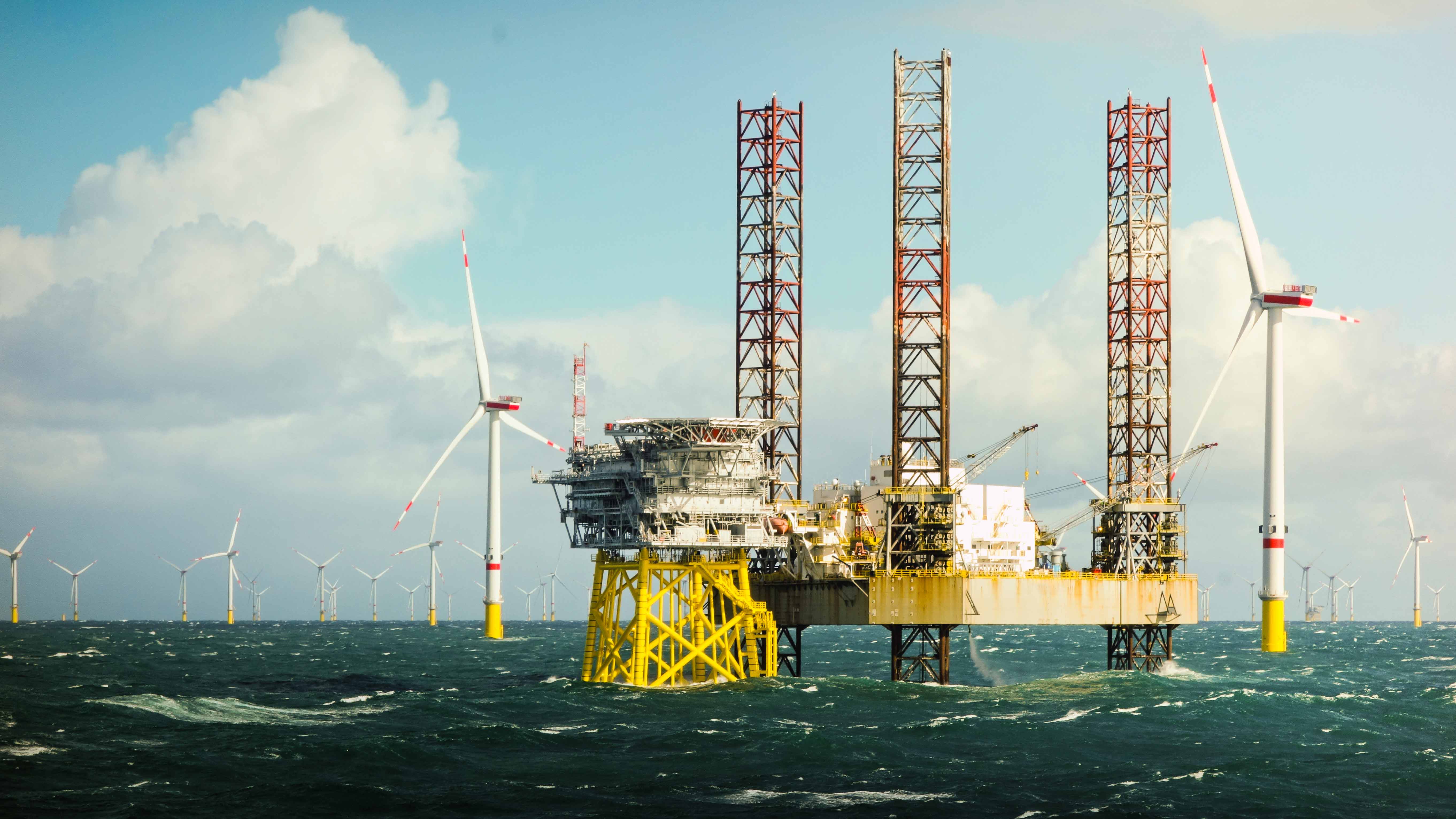 An offshore oil rig with wind turbines in the water.